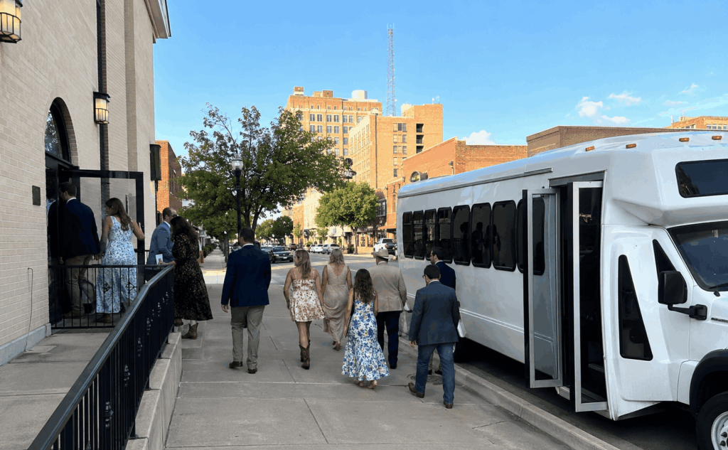 Wedding guests stepping off a shuttle bus near a church ceremony venue in downtown Abilene